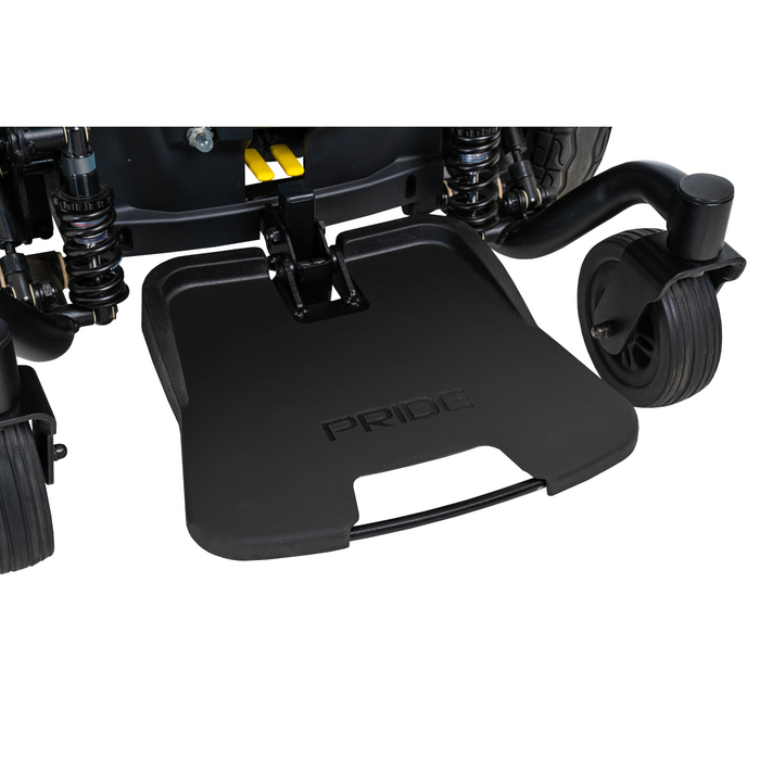 Close-up of a black footrest embossed with PRIDE, attached to the front of a Pride Mobility Jazzy® EVO 614 HD Bariatric Powerchair with ATX Suspension, featuring two small black wheels on each side.
