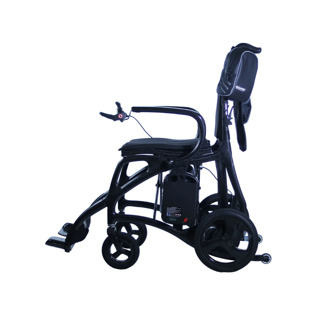 The Journey Air Elite Max Ultralite Carbon Fiber Travel Powerchair features a lightweight curved frame, padded seat, footrest, and a small carry bag attached at the back, displayed against a white background.