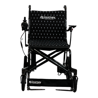 The Journey Air Elite Folding Carbon Fiber Powerchair weighs just 29 lbs and includes a joystick on the right armrest. It features a black design with white dotted seat and backrest, marked with journey on both the backrest and footrest, enhancing its travel-friendly appeal.
