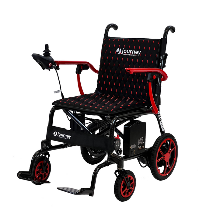 The Journey Air Elite Folding Lightweight Powerchair, weighing only 29 lbs, is black with red accents and features a padded seat for comfort. Easy indoor navigation is supported by the joystick on the armrest and sturdy wheels. The Journey logo adorns the backrest.