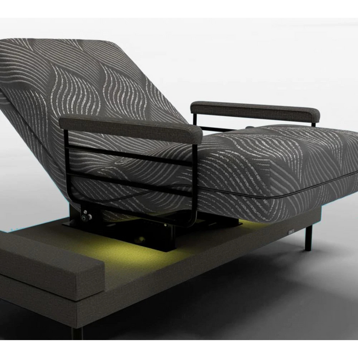 The Journey UPbed® Independence 4-in-1 Motorized Lift Bed features gray patterned fabric, black metal armrests, and sleek design. It partially reclines, emits a soft yellow light underneath highlighting its elegance, and offers a versatile experience on a streamlined base akin to memory foam.