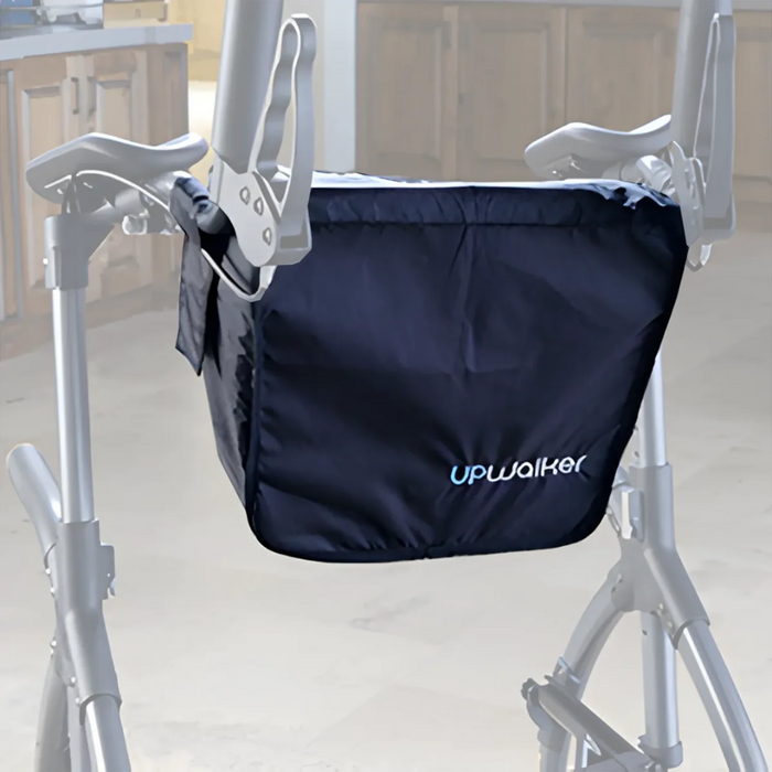 A close-up of a Journey UPWalker with a black storage bag labeled Upwalker, featuring accessories like a sleek beverage holder. The walker is set in a home environment, with kitchen cabinets and countertops visible in the background.