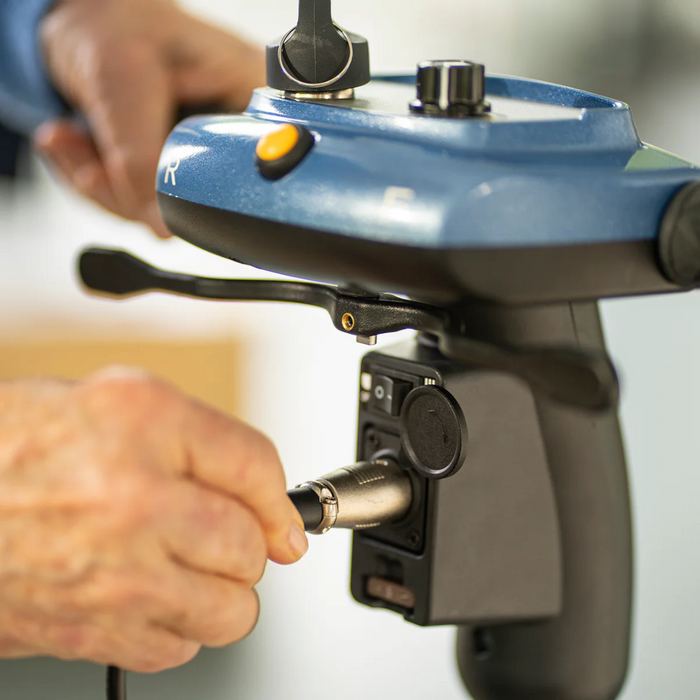 Close-up of hands connecting a cable to a blue and black handheld radio control device with buttons and a dial, likely used for managing machinery like the Journey So Lite® Folding Power Scooter.