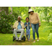 A family strolls through a lush garden. An elderly man smiles from his Journey Zoomer® Portable Travel Powerchair - FAA Approved, accompanied by a young girl holding his arm and a woman in a hat. Flowers and trees surround them.