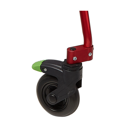 Close-up of a small black caster wheel with a green brake lever, attached to the red frame of a Circle Specialty Klip Pediatric Posterior Walker, isolated on a white background.