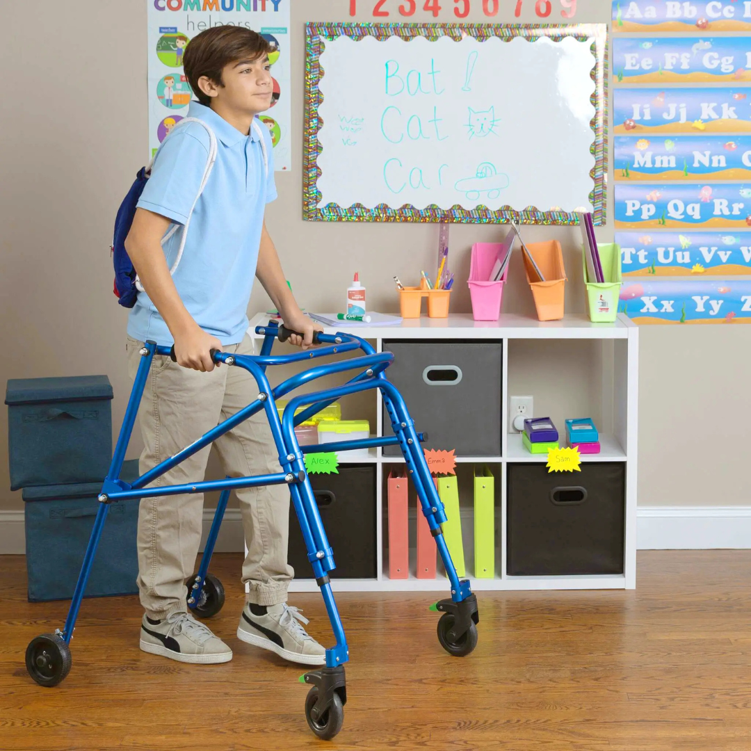 A boy with short hair uses the Circle Specialty Klip Pediatric Posterior Walker in a classroom. He wears a light blue polo, khaki pants, sneakers, and carries a blue backpack. Colorful educational materials are on the walls and shelves.
