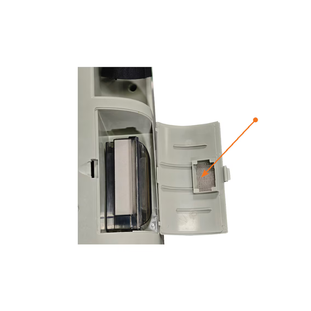 A close-up of an open compartment with an orange arrow pointing to a small rectangular mesh filter inside the door, which is part of the Accessoires For Rhythm LM10A O2 Concentrators. This filter is a crucial oxygen concentrator part that helps maintain optimal performance.