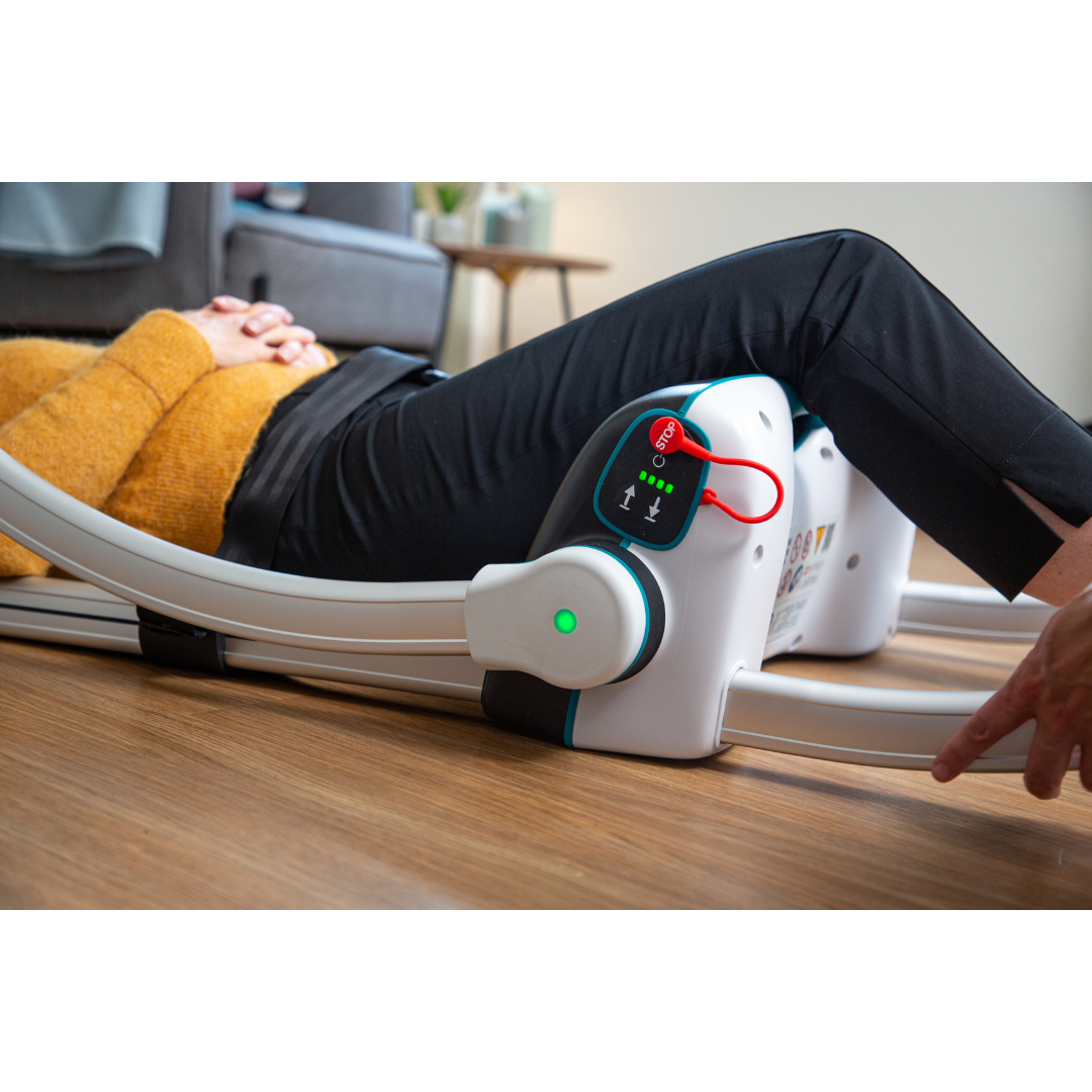 A person lies on the floor using the LiftUp Raizer II, following the user manual to get up. With knees bent and hands on their stomach, they activate the device, which emits a green light during operation.