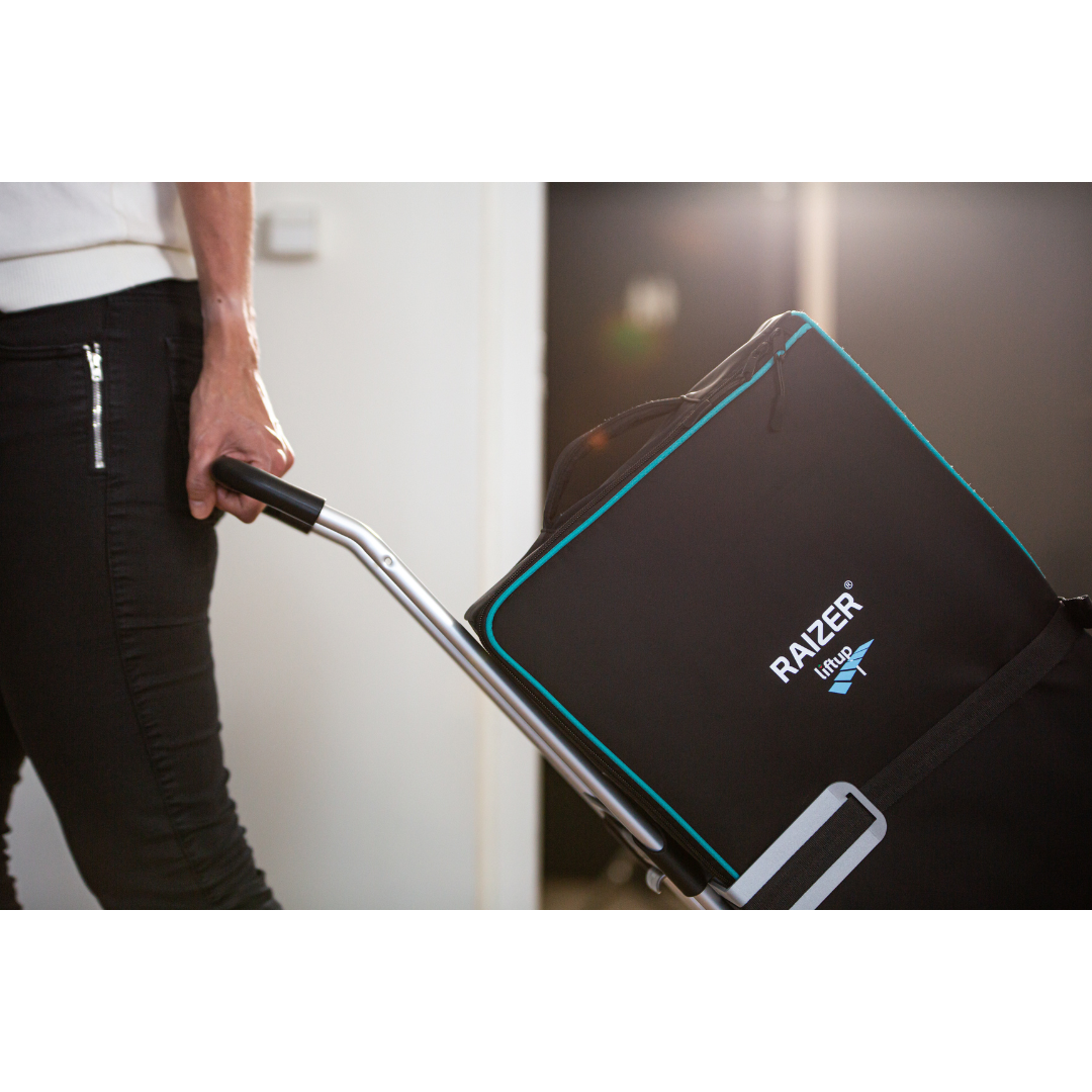 A person in black pants pulls a cart carrying a large black bag with blue trim indoors, possibly transporting a LiftUp Raizer II product brochure or user manual.