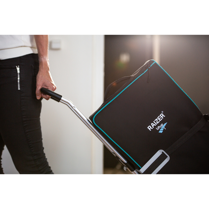 A person in black pants pulls a cart carrying a large black bag with blue trim indoors, possibly transporting a LiftUp Raizer II product brochure or user manual.