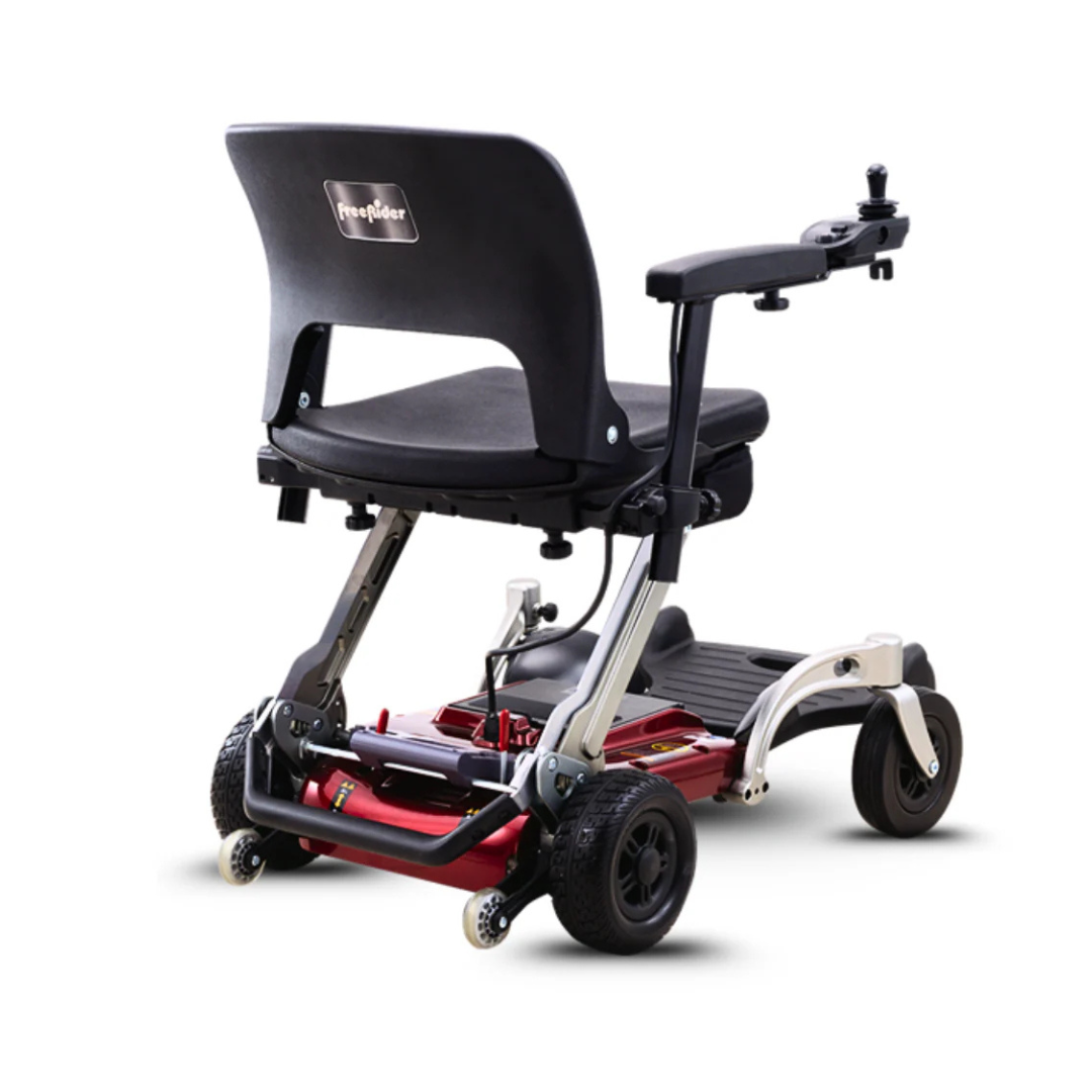 The FreeRider Luggie Travel Lightweight Powerchair features a sleek red and silver compact frame, black cushioned seat with armrests, and four wheels, shown from the back against a white background.