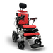 The ComfyGo MAJESTIC IQ-9000 is a red and black electric wheelchair with quilted seat and backrest, featuring an auto-reclining function. It includes a headrest, armrests with digital joystick controller, footrests, and a metallic frame housing brushless silent motors for smooth mobility on four wheels.