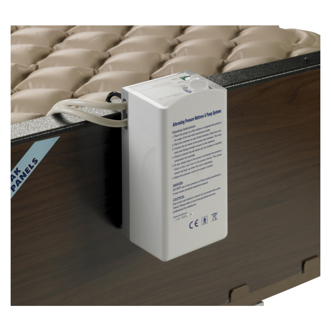 A Drive Med-Aire Alternating Pressure Pump and Pad System control unit, in white, is attached to a hospital bed with a wood-look panel. It has a dial, indicator lights, and printed instructions on the front.