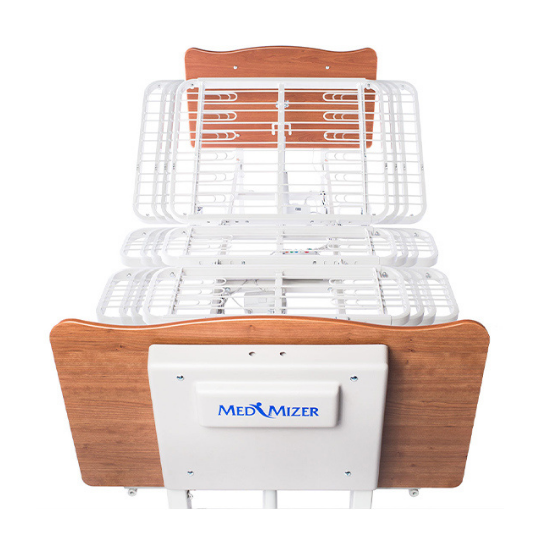 The Med-Mizer EX8000 ComfortWide Bariatric Width Adjusting Electric Bed features a white metal frame, wooden headboard and footboard (with the Med-Mizer logo), and a segmented design for adjustable patient positioning.