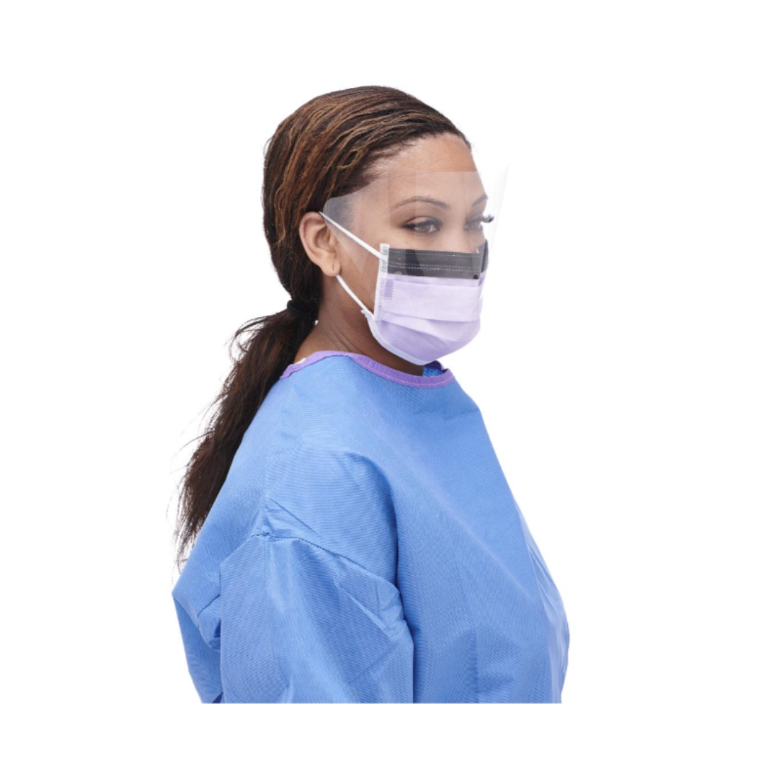 A woman in a blue medical gown wears the Medline ASTM L3 Procedure Face Mask with Eye Shield and Ear Loops, along with a clear face shield, standing slightly left against a white background.