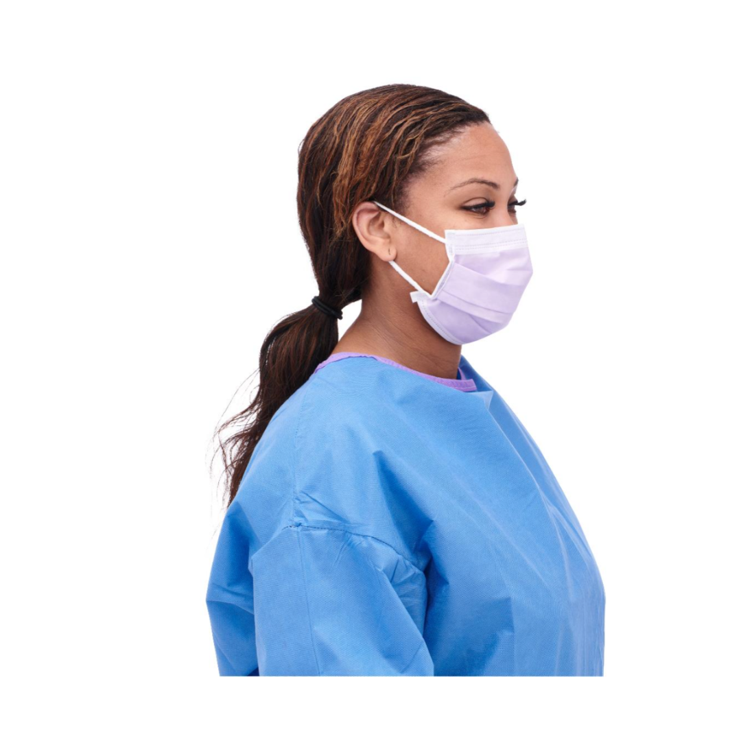 A woman in a blue medical gown and Medline ASTM Level 3 Procedure Face Mask with ear loops, shown in profile with her hair tied back, stands against a white background.