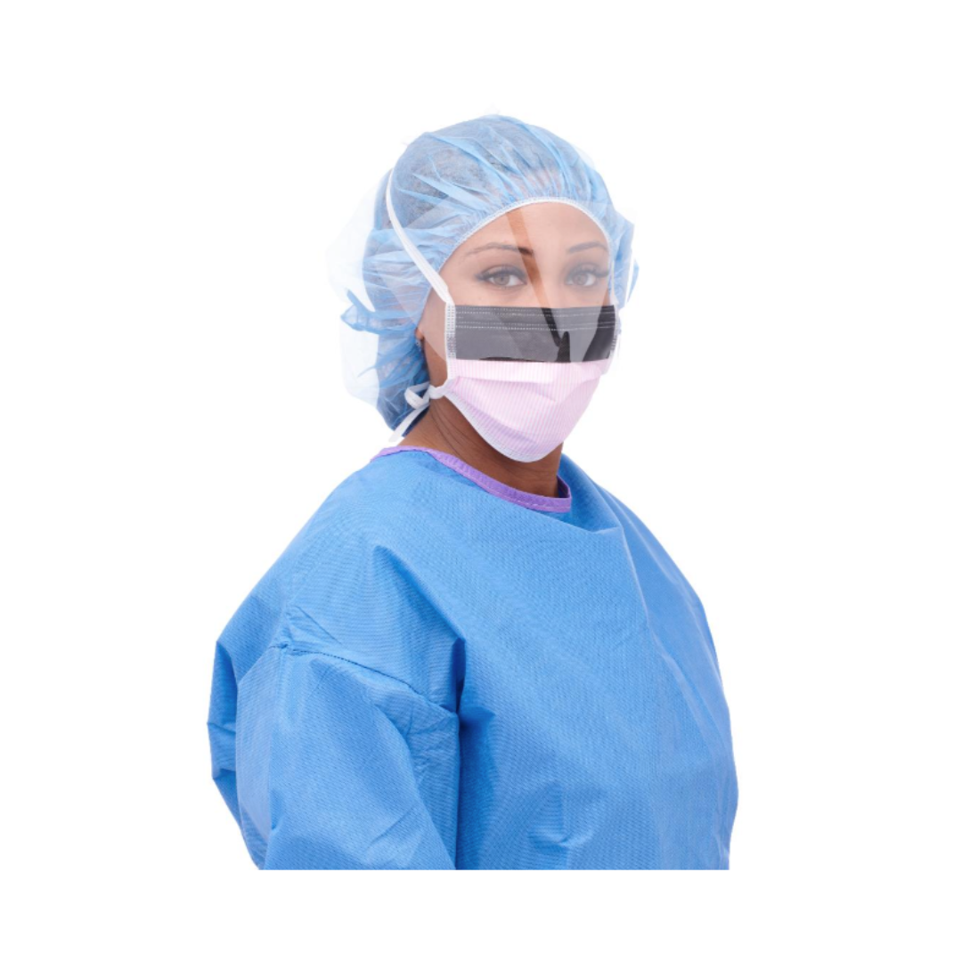 A person wearing a blue surgical gown, hair cover, and Medline ASTM Level 3 Surgical Face Mask with Eye Shield looks toward the camera, appearing to be a healthcare worker prepared for a sterile medical environment.