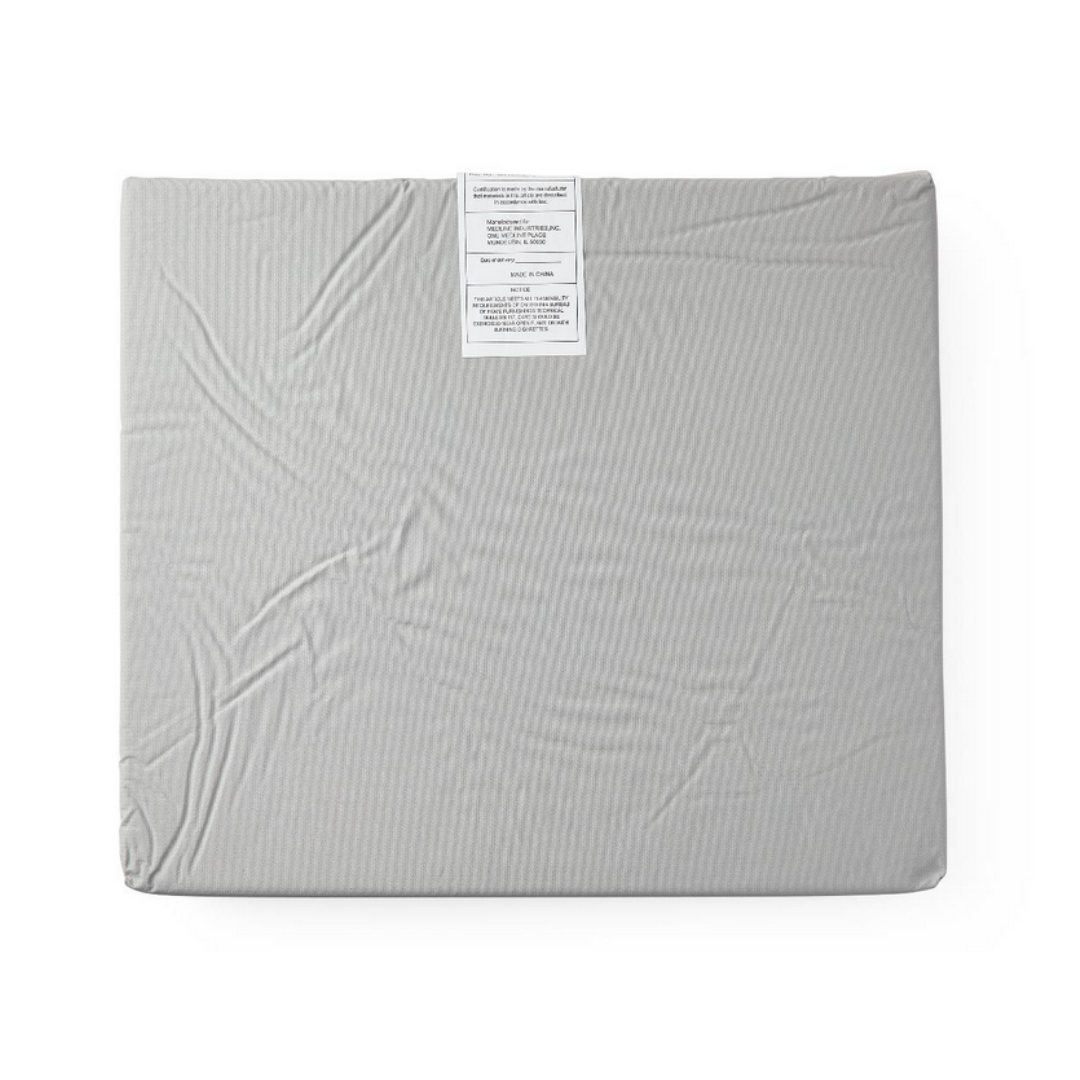 The Medline Comfort Foam Cushions - 3 Thickness is a rectangular gray wheelchair cushion with a fabric top, slight wrinkles, and two white care labels at the top edge, designed for pressure relief.