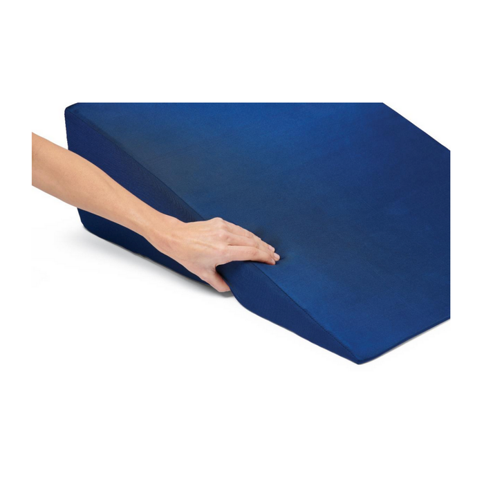 A hand presses into the Medline High-Density Foam Bed Wedge (24 x 20 x 8.5), showcasing its softness and flexibility on a white background. The dark blue, wedge-shaped cushion offers versatile elevation for multiple needs.