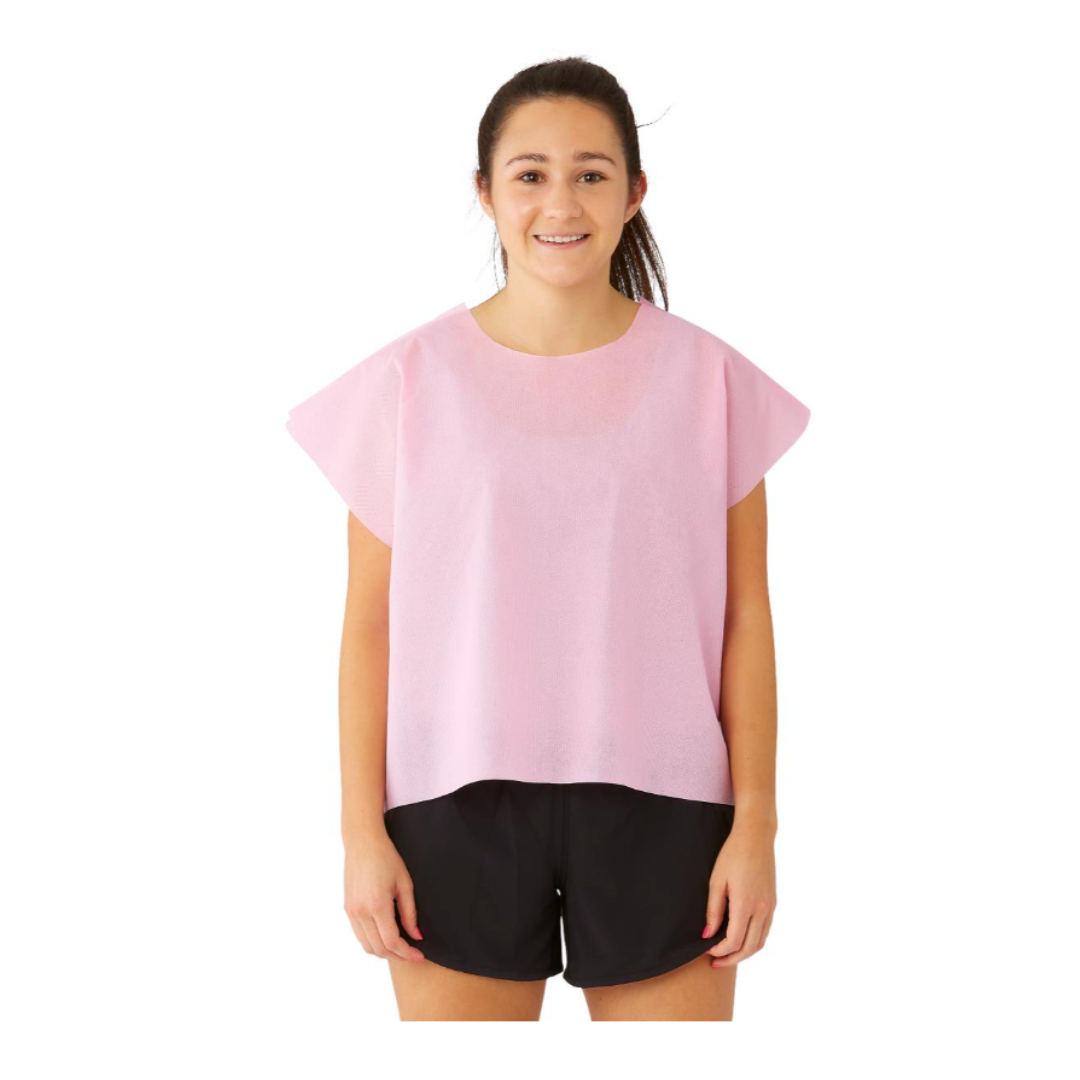 A young woman smiles facing forward, wearing a Medline Disposable Multilayer Patient Cape (30" x 21") in light pink over black shorts, with a plain white background.