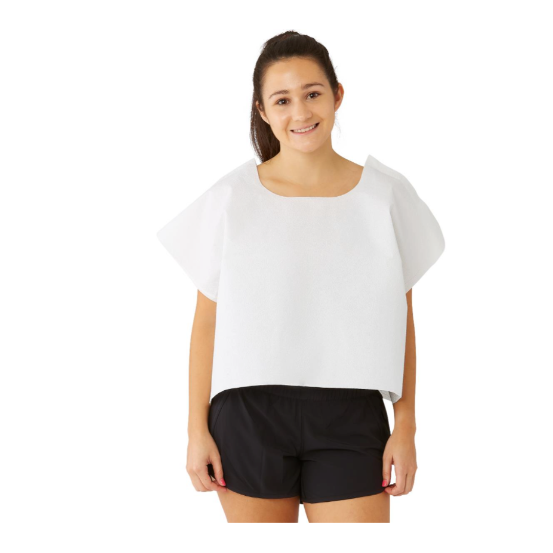 A young woman stands and smiles against a white background, wearing a Medline Disposable Exam Cape (30" x 21", Tissue Poly Tissue) over black shorts.