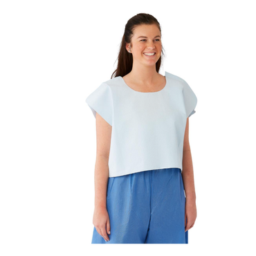 A woman with long brown hair, in a light blue sleeveless top and blue pants, smiles against a white background, evoking the comfort of Medline Disposable Exam Capes 30" x 21" | Tissue Poly Tissue Gown during medical visits.