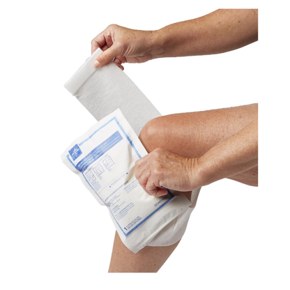 A person applies the Medline Instant Cold Pack with Self-Adhering Wrap, 5" x 9", on their bent knee, demonstrating easy application and effective cooling for wound care.