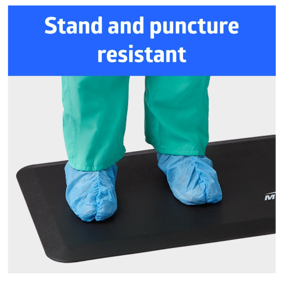 A person in teal pants and blue shoe covers stands on a Medline Standard Bio-Foam Anti-Fatigue Floor Mat (20" x 48") with "Stand and puncture resistant" text at the top. This mat offers comfort and durability while you work.