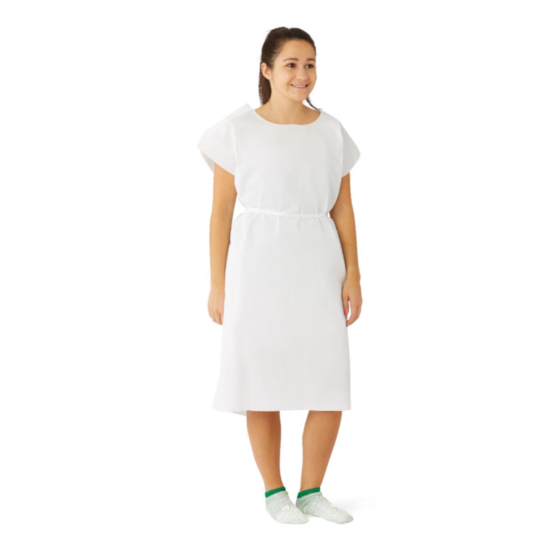 A woman smiles while standing in a Medline Reinforced Tissue Patient Gown with green and white non-slip socks against a plain white background.