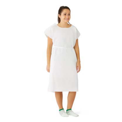 A woman smiles while standing in a Medline Reinforced Tissue Patient Gown with green and white non-slip socks against a plain white background.