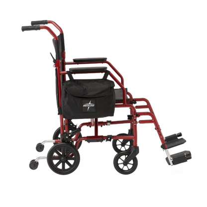 A Medline Steel Transport Chair with Wide 19" Seat, shown in red with black armrests, footrests, and a side storage bag, is displayed from the side against a white background.