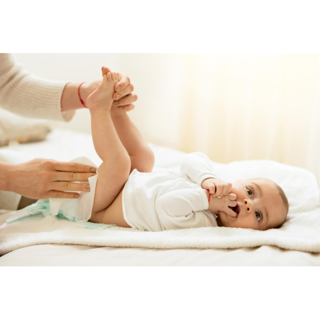 During a diaper change, an adult gently holds a baby's legs while using Medline Ultrasoft Disposable Dry Cleansing Cloths. The baby lies on a soft blanket, looking up with fingers in its mouth.