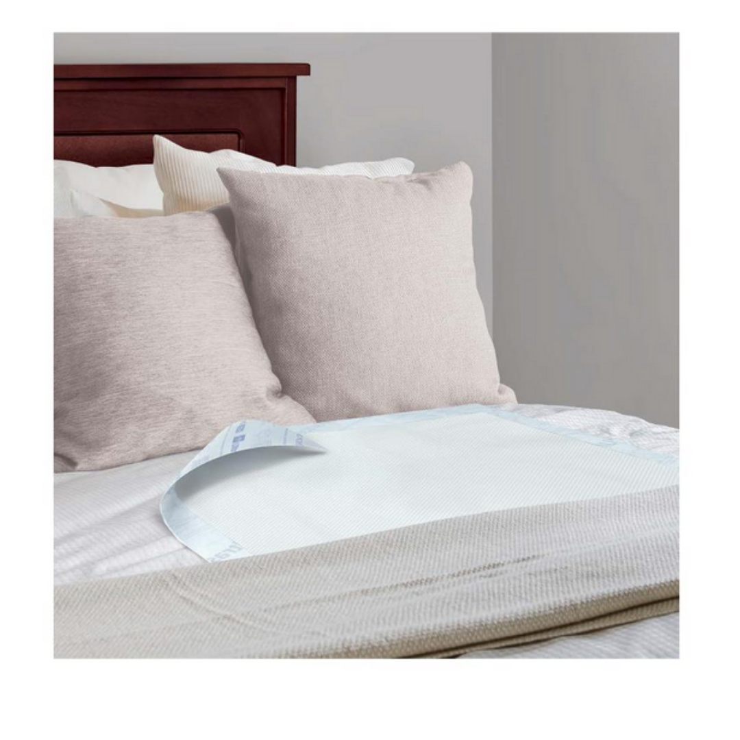 A neatly made bed with beige pillows and a wooden headboard displays a Medline Ultrasorbs Advanced Premium Underpad (30 x 36) atop the sheets near the foot, offering advanced incontinence management. The room has light-colored walls.