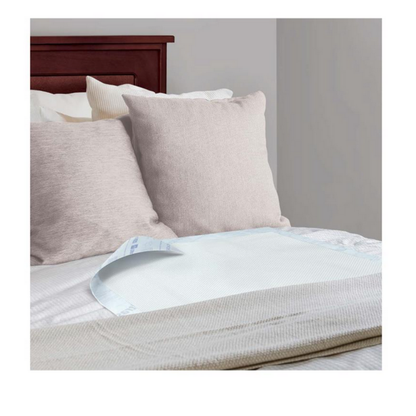 A neatly made bed with beige pillows and a wooden headboard displays a Medline Ultrasorbs Advanced Premium Underpad (30 x 36) atop the sheets near the foot, offering advanced incontinence management. The room has light-colored walls.