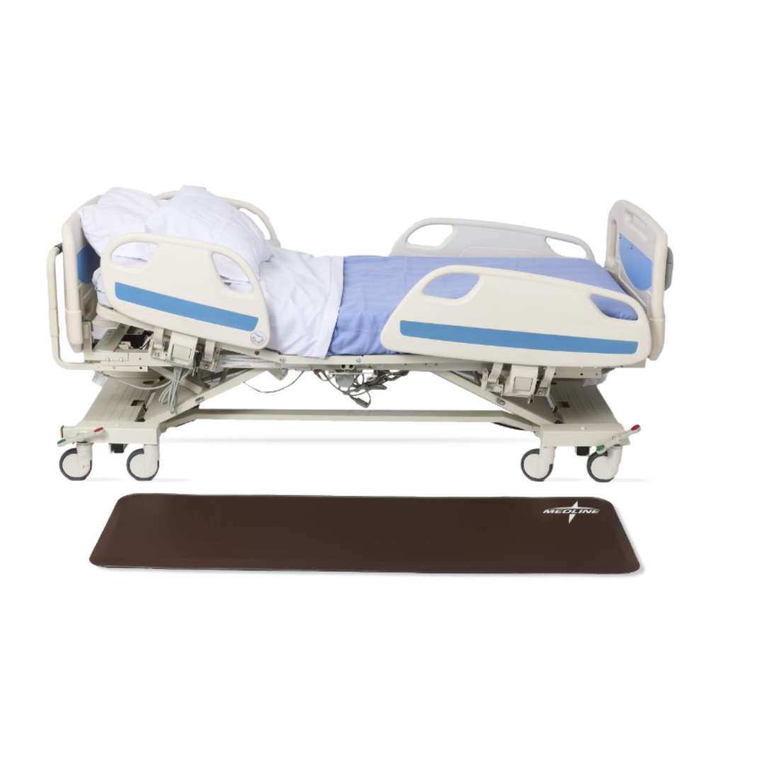 A hospital bed is positioned at an angle with its head and foot raised. On the floor in front of it lies a brown Medline Beveled Edge Bedside Fall Mat—see spec table for more product details and specifications.