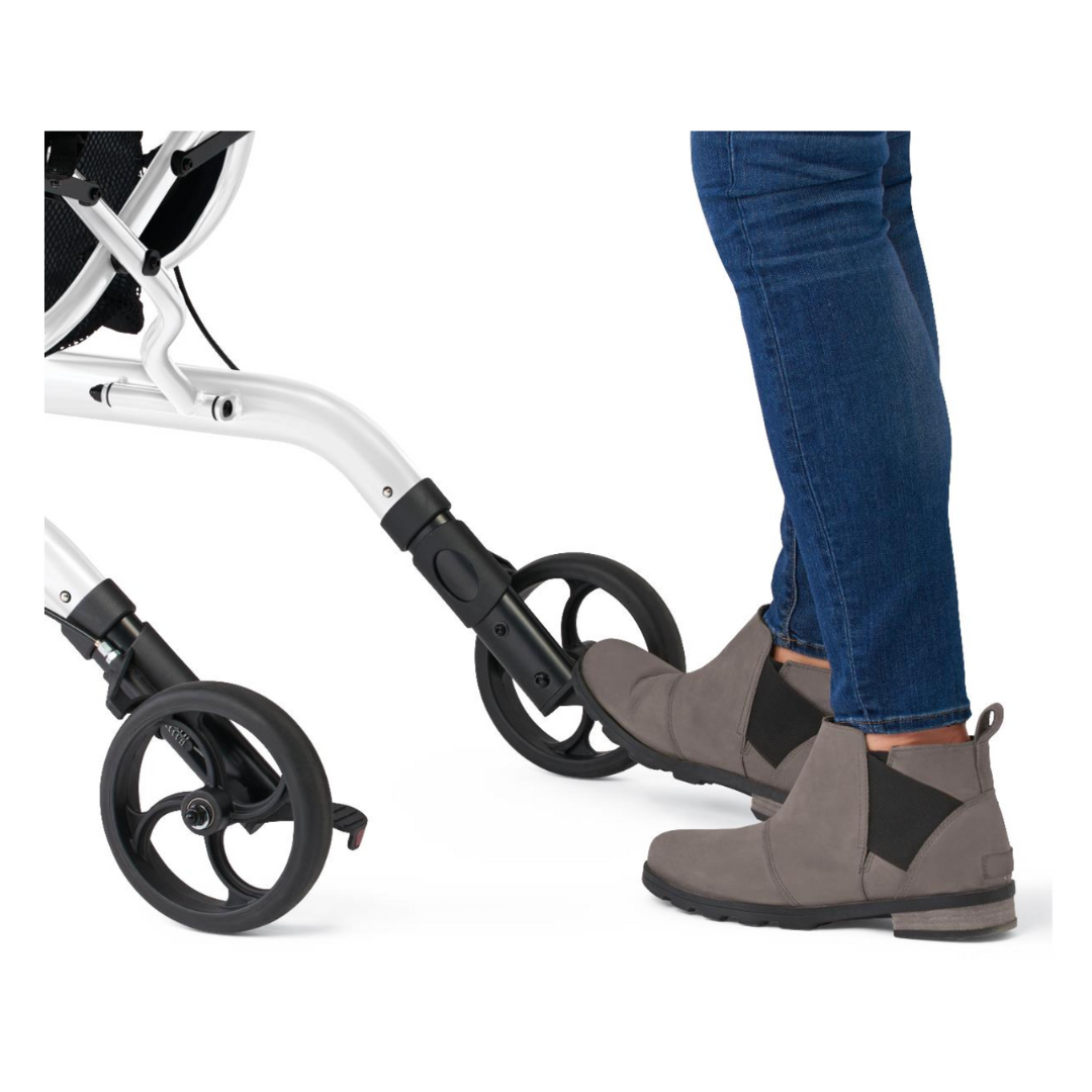 A person wearing gray ankle boots and blue jeans uses their foot to press the brake on a Medline European-Style Aluminum Ultralite Rollator with black wheels.
