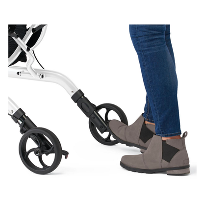 A person wearing gray ankle boots and blue jeans uses their foot to press the brake on a Medline European-Style Aluminum Ultralite Rollator with black wheels.