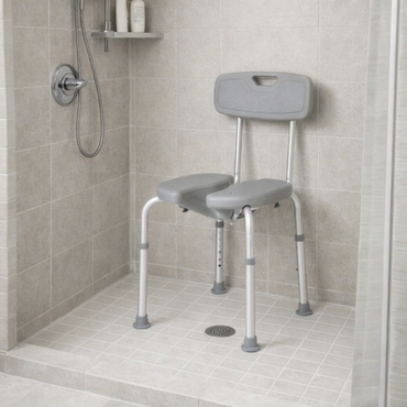 The Medline Knockdown Shower Chair with Cutout, featuring a gray split seat and backrest, stands in a modern walk-in shower with tiled floor, wall-mounted handheld showerhead, toiletries shelf, and contemporary design touches.