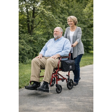 A smiling woman pushes an older man in a red Medline Steel Transport Chair with Wide 19" Seat along a paved park path surrounded by green trees.