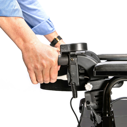 A person in a blue shirt grips the handle of the Miracle Mobility Portable 4N1 Walker Wheelchair Combo, adjusting a lever. The background is white and uncluttered.