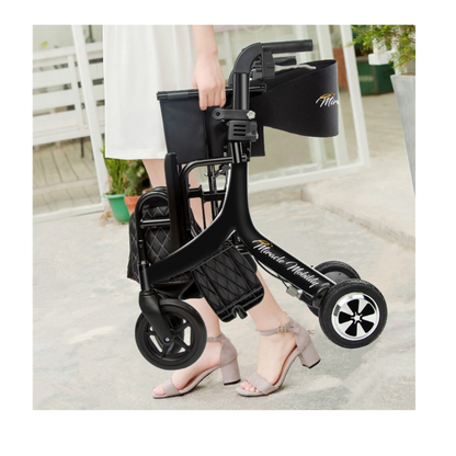 A woman in a white dress and heeled sandals carries the Miracle Mobility Portable 4N1 Walker Wheelchair Combo with a side bag, standing outdoors on a concrete path near a building.