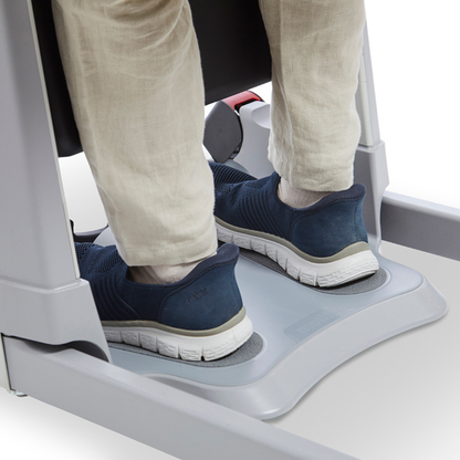 A person wearing light pants and navy blue sneakers stands on the footplates of a gray Molift Transfer Pro - Innovative Sit-To-Stand Patient Lift, a device designed for smooth and secure patient movement.