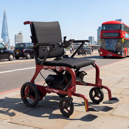 The Monarch Flyer Ultra-Lite Carbon Powerchair sits on a London sidewalk near a red double-decker bus, with the Shard in view. Discover specs and videos at our website.