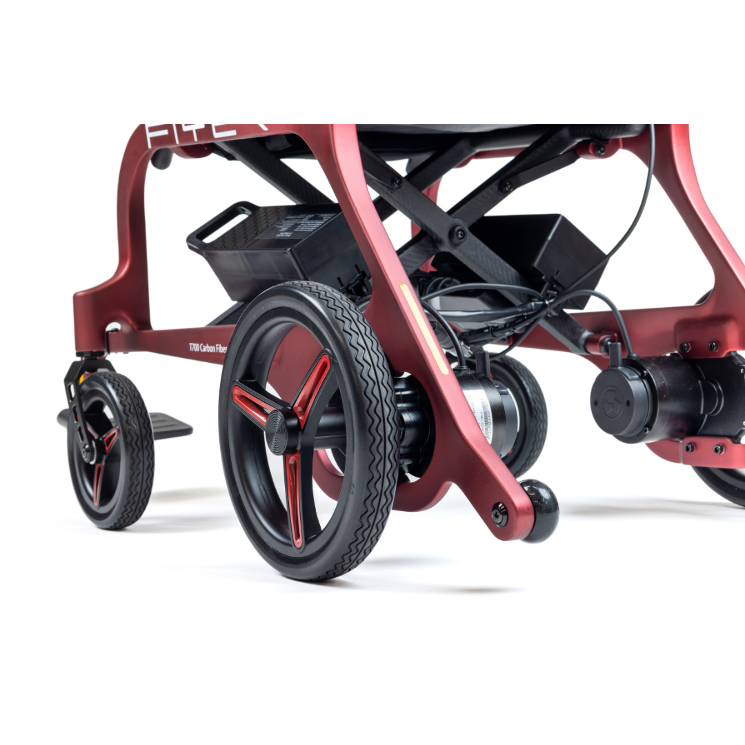 Close-up of the wheel and mechanical parts of the Monarch Flyer Ultra-Lite Carbon Powerchair, highlighting its suspension, motor, and battery against a white background. See specifications and warranty details for more information.