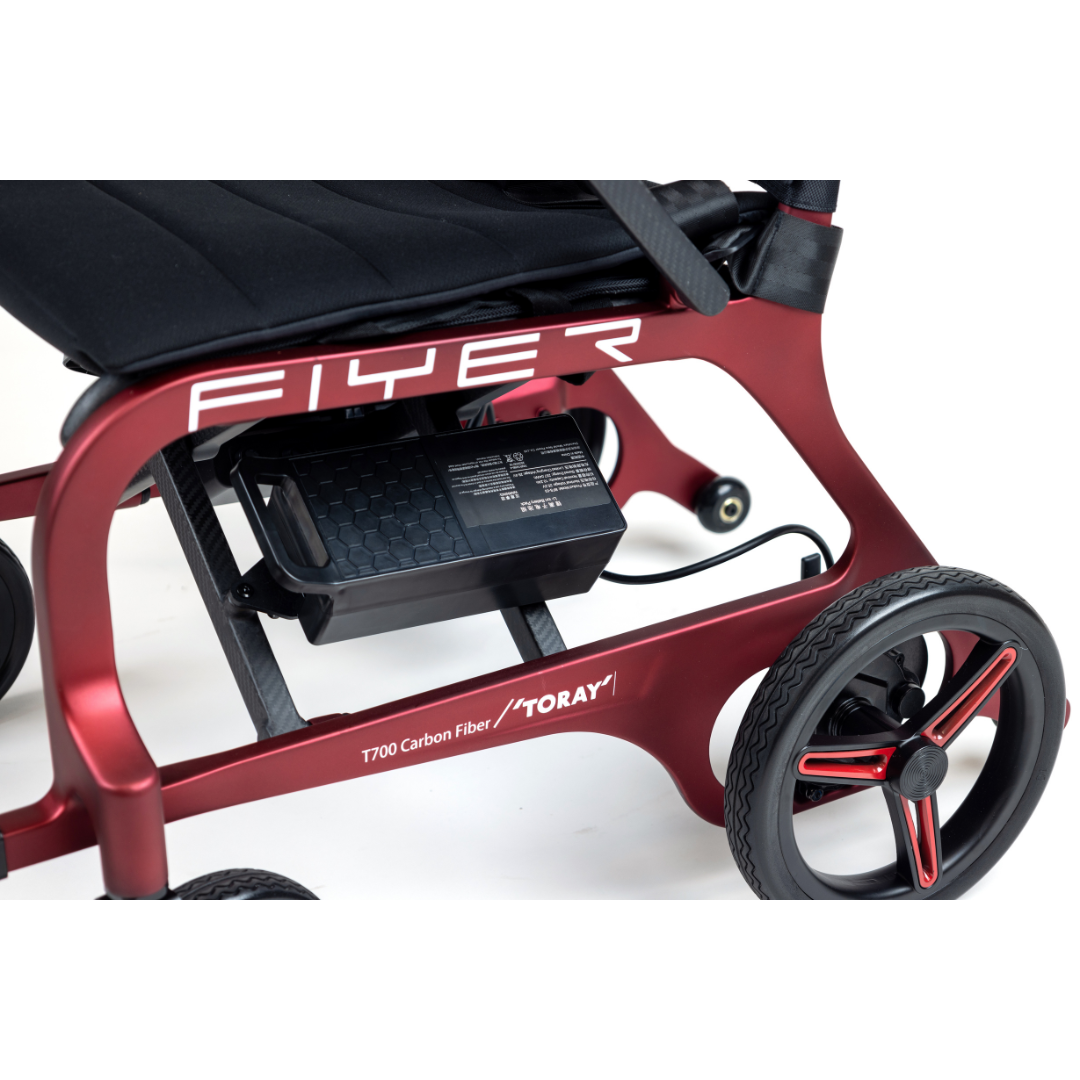 Close-up of the Monarch Flyer Ultra-Lite Carbon Powerchair in red, featuring the rear wheel, seat, and a black battery pack under the frame. Visit our site for specs and warranty info.