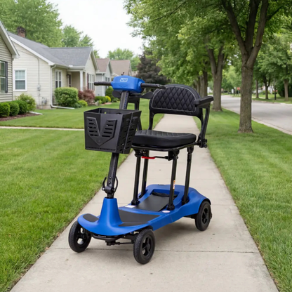 A Monarch Genie Ultralight Portable Mobility Scooter with a blue frame, black seat, and basket is parked on a suburban sidewalk surrounded by green lawns, trees, and houses; only CSS code appears in the product description.