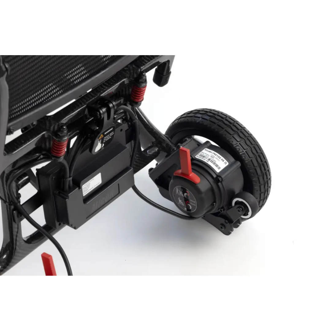 Close-up of the underside of the Monarch MM60 Carbon Ultralite Electric Wheelchair, showing a battery pack, red suspension springs, wiring, and a rear wheel with an attached motor.