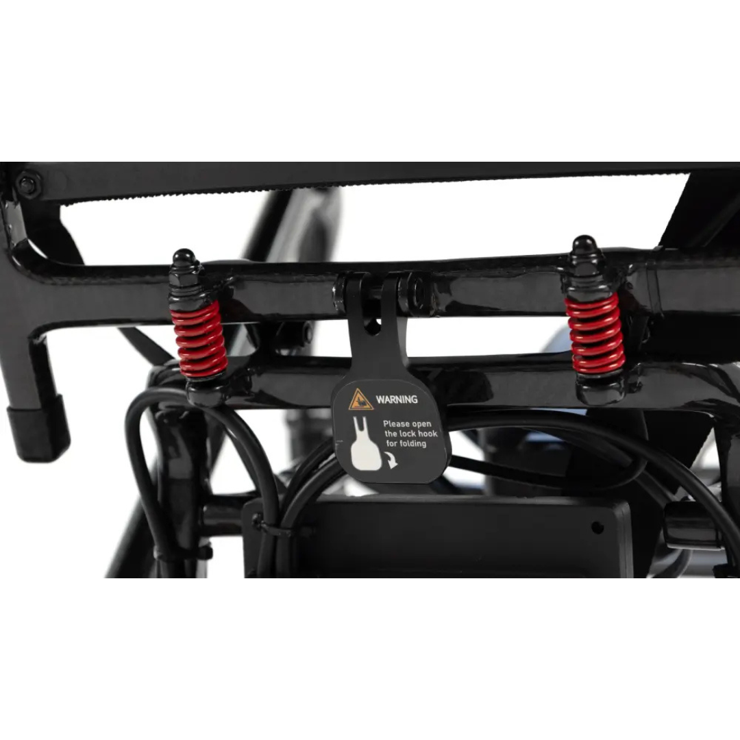 Close-up of a bicycle frame showing two red suspension springs and a warning label instructing to open two lock hooks for folding—similar to the practical mechanisms found on ultra-lightweight folding mobility devices such as the Monarch MM60 Carbon Ultralite Electric Wheelchair. Black wires are visible near the locking mechanism.