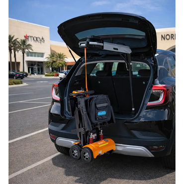 A Monarch Atlas 4 Portable Car Lift is attached to a black SUV’s open trunk in a parking lot, lifting an orange mobility scooter. Macy's and Nordstrom stores are visible in the background; no product description text appears.