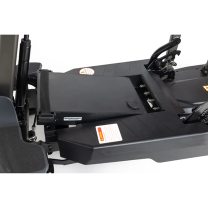 Close-up of the Monarch Genie Auto Folding Portable Scooter's black battery compartment, with the battery partially removed to show detailed labels and deck mechanisms for easier maintenance and enhanced safety.